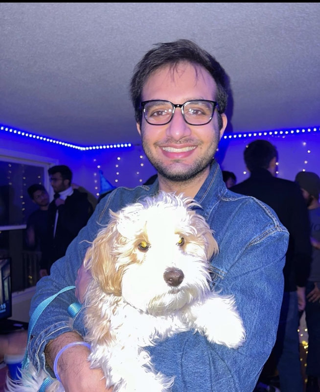a colour photograph of a man looking at the camera smiling and holding a small white dog.