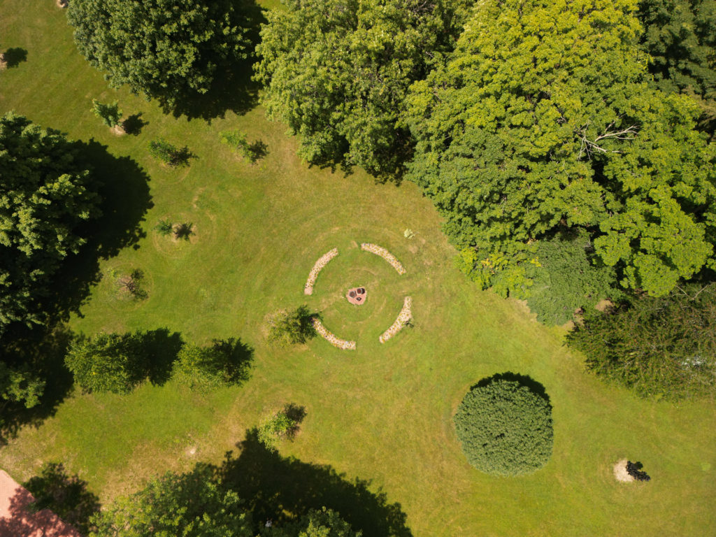 Color aerial photo of a circle shaped from flower beds on a lawn in a grove of trees.